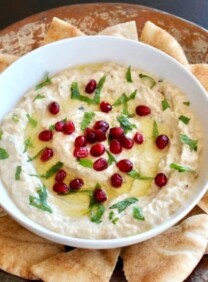 Overhead shot of Roasted Eggplant Yogurt Dip topped with pomegranate arils and fresh mint, on a platter with pieces of pita.