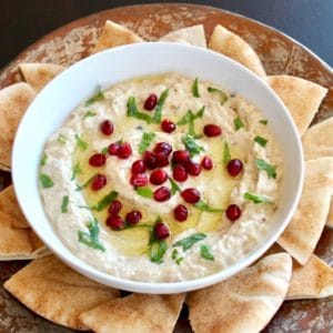 Overhead shot of Roasted Eggplant Yogurt Dip topped with pomegranate arils and fresh mint, on a platter with pieces of pita.