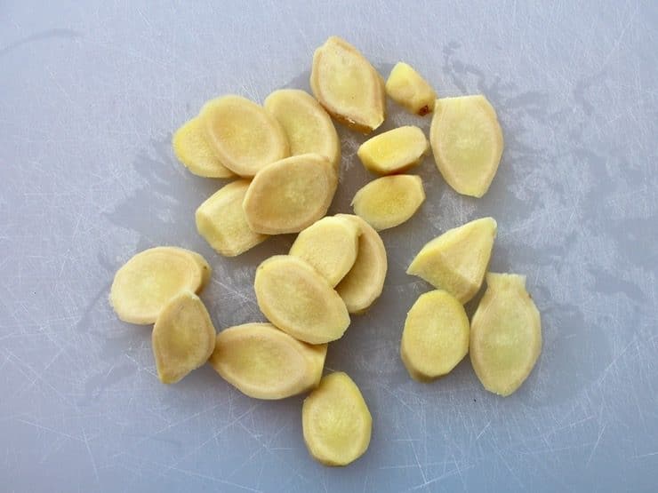 Sliced peeled ginger pieces on white cutting board.