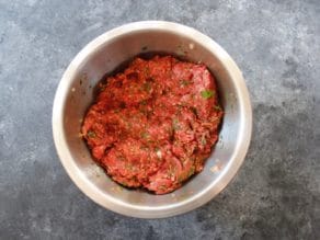 Ground meat mixed with spices in a metal bowl