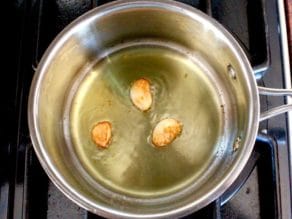 Three cloves of pan-roasted garlic, golden brown, in olive oil in saucepan.