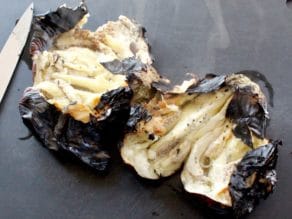 Flame roasted eggplant on cutting board, cut open, revealing steaming eggplant flesh inside.