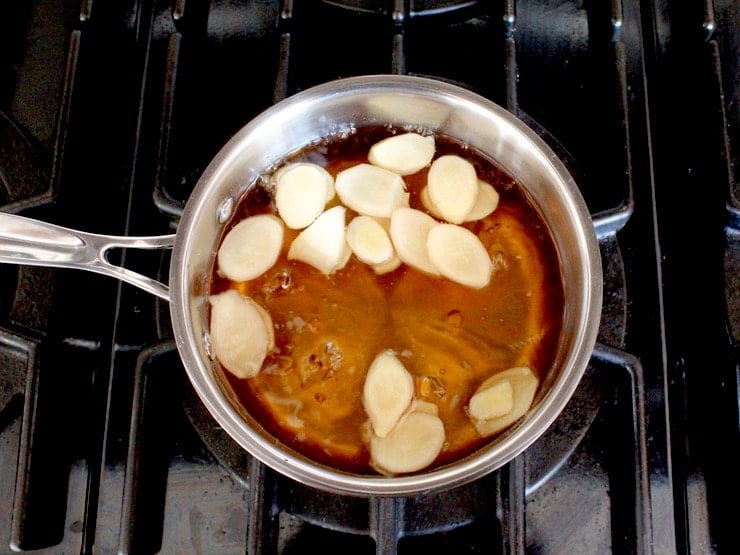Slices of ginger in saucepan with agave water simmering on stovetop.