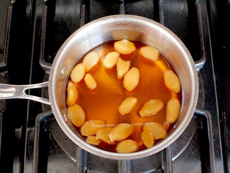 Softened slices of ginger in saucepan, cooling in syrup on stovetop.