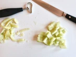 Seeded cucumber chunks with knife and seeding tool on white cutting board.