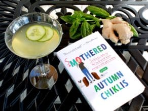 Smothered by Autumn Chiklis book on black metal table outdoors with Cucumber Ginger Martini, basil and ginger in background.