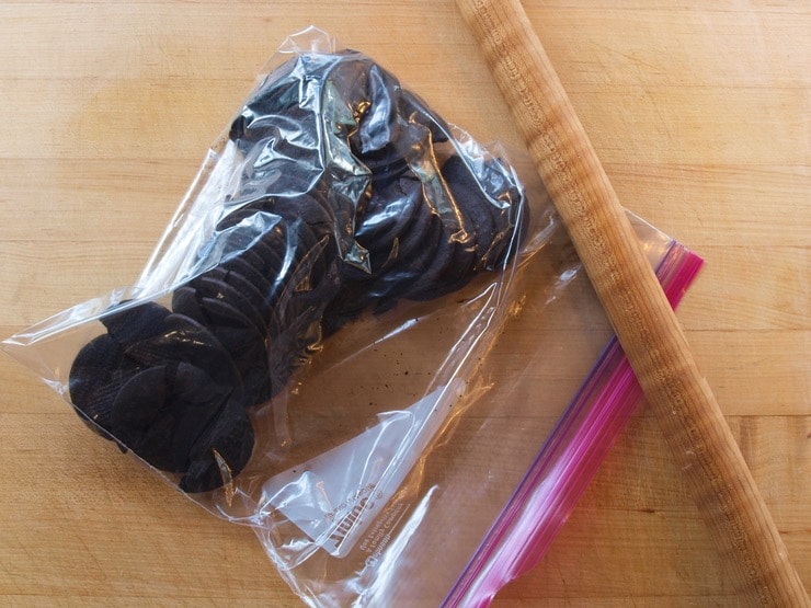 Reusable plastic storage bag filled with chocolate cookies next to a wooden rolling pin.