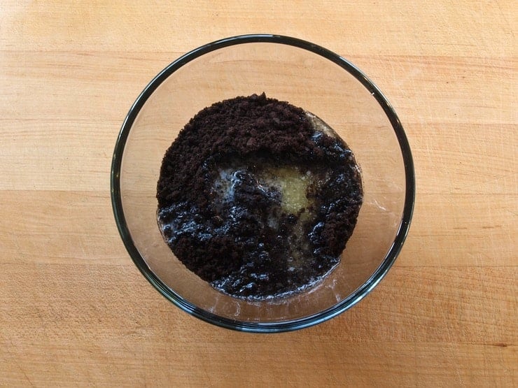 Crushed chocolate cookies in a clear glass mixing bowl.