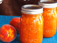 Two jars of Peach Saffron Preserves and peaches on a blue tablecloth, showcasing the delicious peach jam