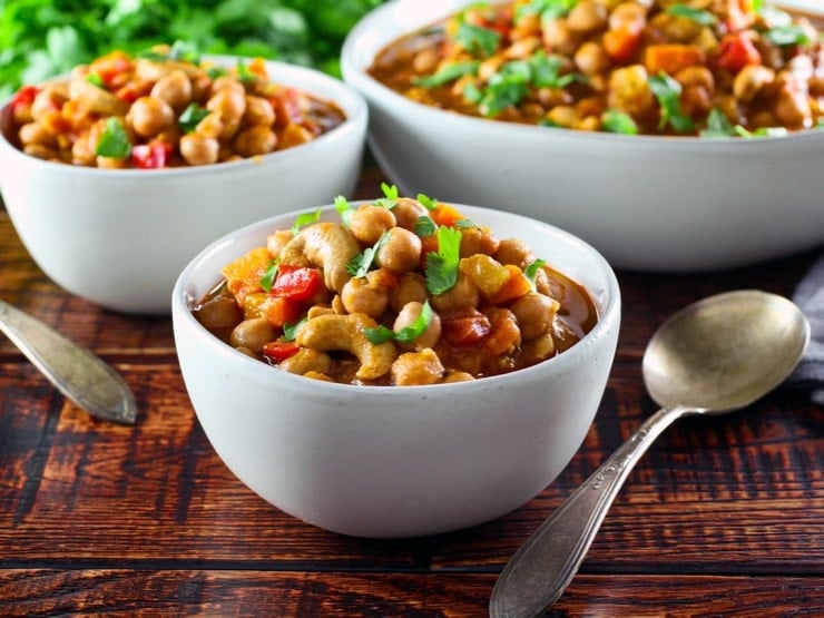 Three white bowls filled with vegan chickpea chili on a wooden table.