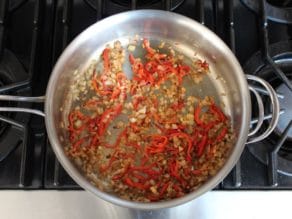Sauteed diced onion with sliced roasted bell pepper in saute pan on stovetop.