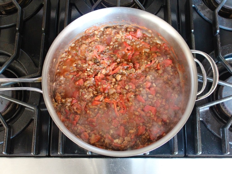 Lentil, pepper and mushroom mixture cooked steaming hot in saute pan on stovetop.