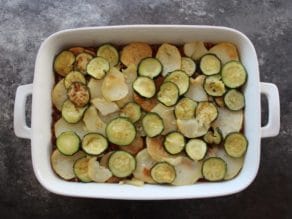 Layered sliced potatoes and zucchini in 2 quart casserole dish on concrete surface.