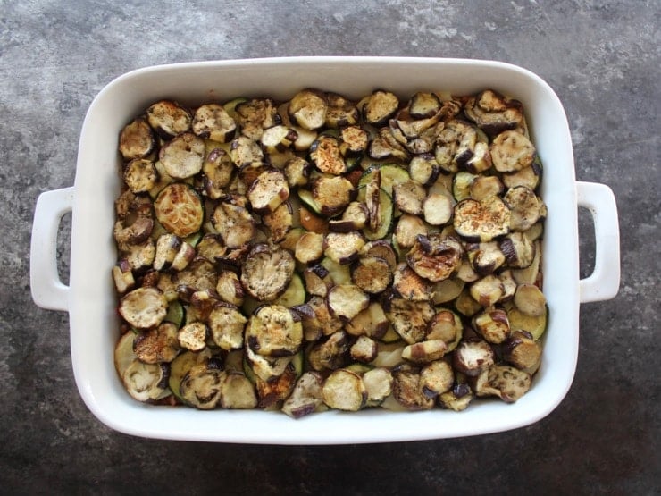 Roasted eggplant slices layered in 2 quart casserole dish on concrete surface.