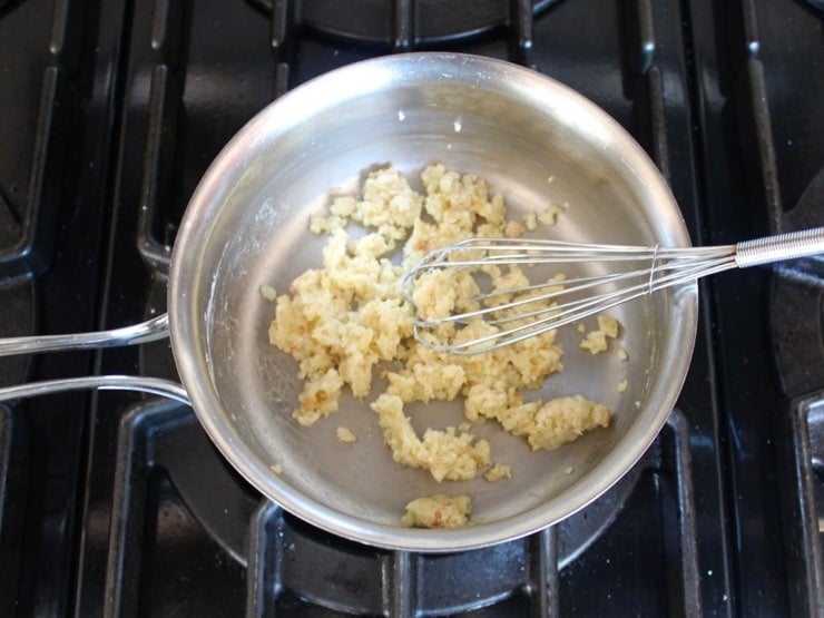 Whisking together flour, onion and fat in small saucepan on stovetop.