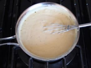 Whisking together thickened hummus topping sauce in saucepan on stovetop.