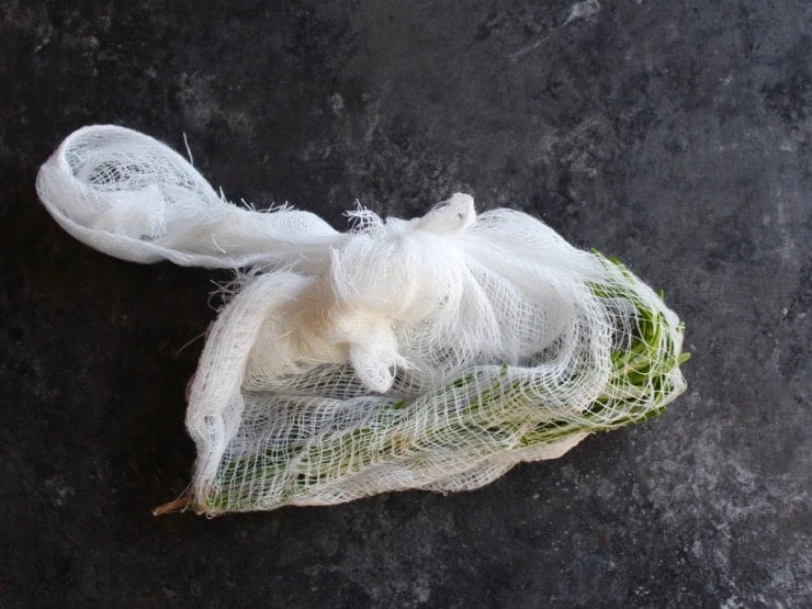 Rosemary sprigs wrapped in cheesecloth tied in a bundle on concrete background.