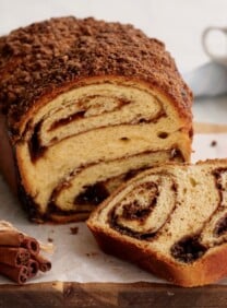 Featured - Cinnamon Babka sliced on cutting board with cinnamon stick bundle. coffee and towel in background.