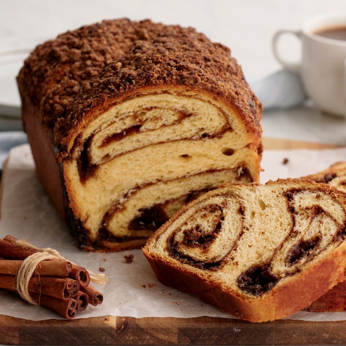Featured - Cinnamon Babka sliced on cutting board with cinnamon stick bundle. coffee and towel in background.
