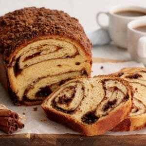 Horizontal image - Cinnamon Babka sliced on cutting board with cinnamon stick bundle. coffee and towel in background.