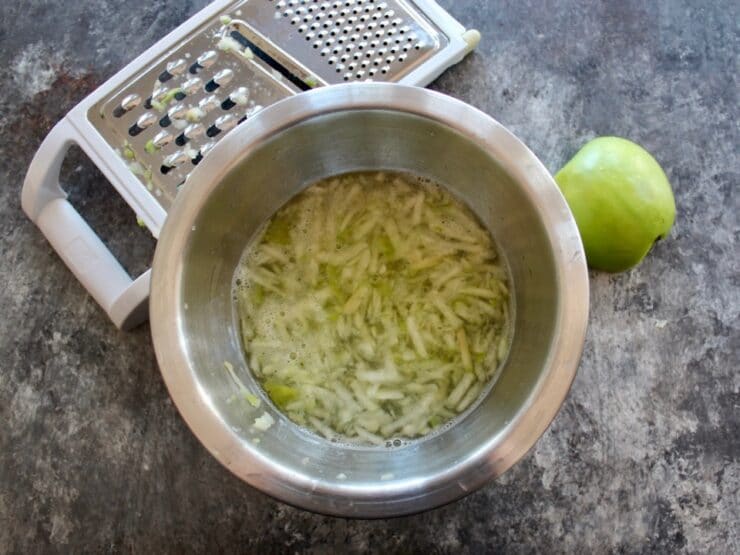 Overhead shot of chopped green apple pieces soaking in water in a metal mixing bowl.