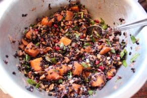 Overhead shot of black rice mixed with butternut squash, chopped fruit and fresh mint in a metal mixing bowl.