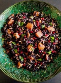 Overhead shot of black rice mixed with butternut squash, chopped fruit and fresh mint in a green decorative bowl.