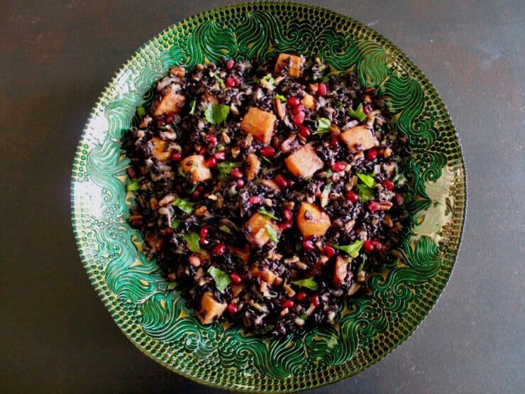 Overhead shot of black rice mixed with butternut squash, chopped fruit and fresh mint in a green decorative bowl.