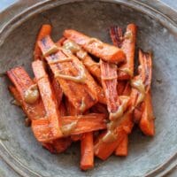 Horizontal shot of rustic tray of roasted carrots with tahini drizzle.