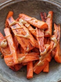 Horizontal shot of rustic tray of roasted carrots with tahini drizzle.