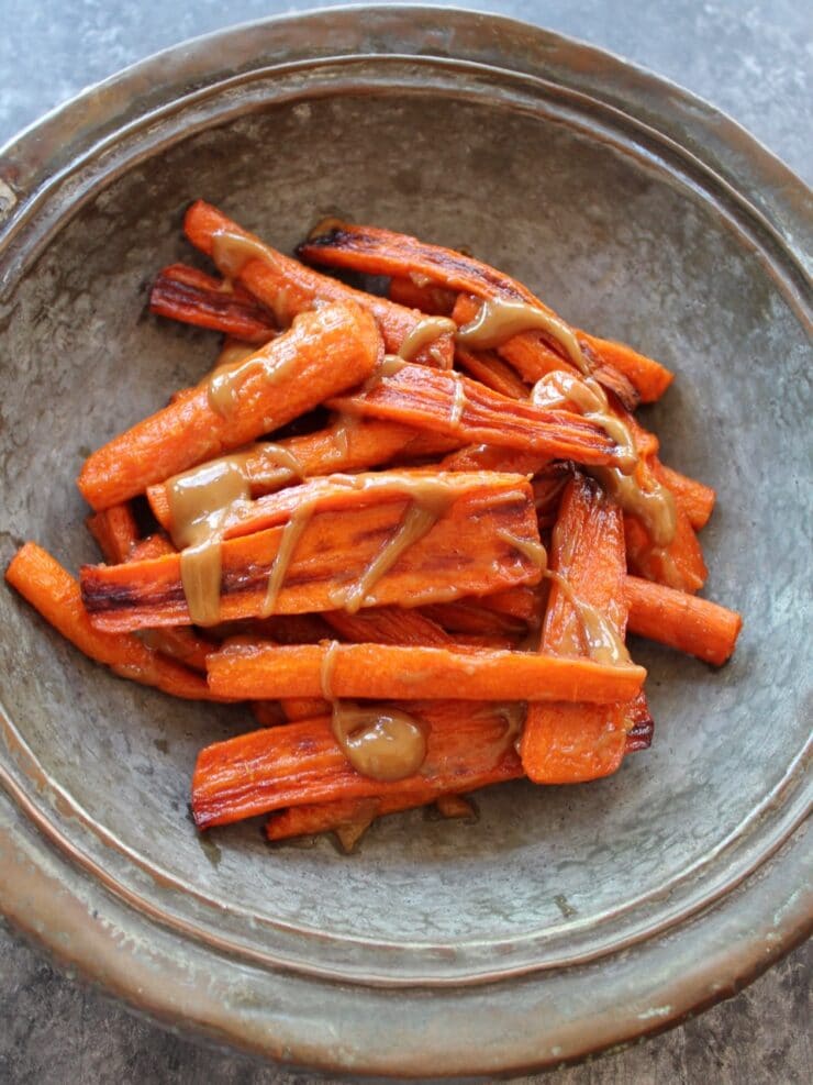 Vertical shot of rustic tray of roasted carrots with tahini drizzle.