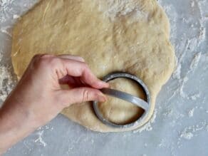 A circular dough cutter pressing into raw sufganiyot dough.