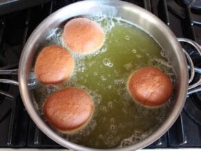 Four sufganiyot floating and frying in a large pot of hot cooking oil.