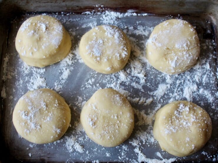 A cooking sheet with 6 circles of uncooked sufganiyot dough, dusted with flour.