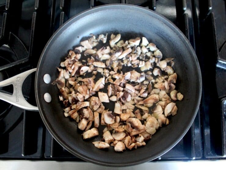 Raw diced mushrooms in nonstick skillet starting to sear on stovetop.