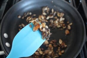 Blue silicone spatula showing golden brown mushroom pieces in close up to camera, skillet of mushroom pieces in background.