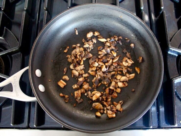 Seared diced mushrooms in black nonstick skillet on stovetop.