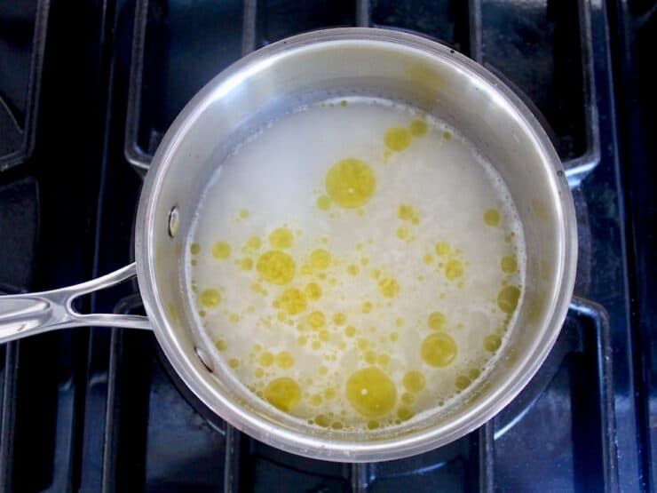 Small saucepan with basmati rice, water and olive oil starting to simmer on stovetop.