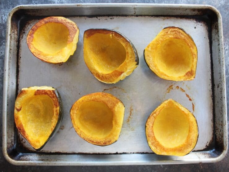 Baking sheet of roasted acorn squash halves with golden brown edges, flesh side facing upward