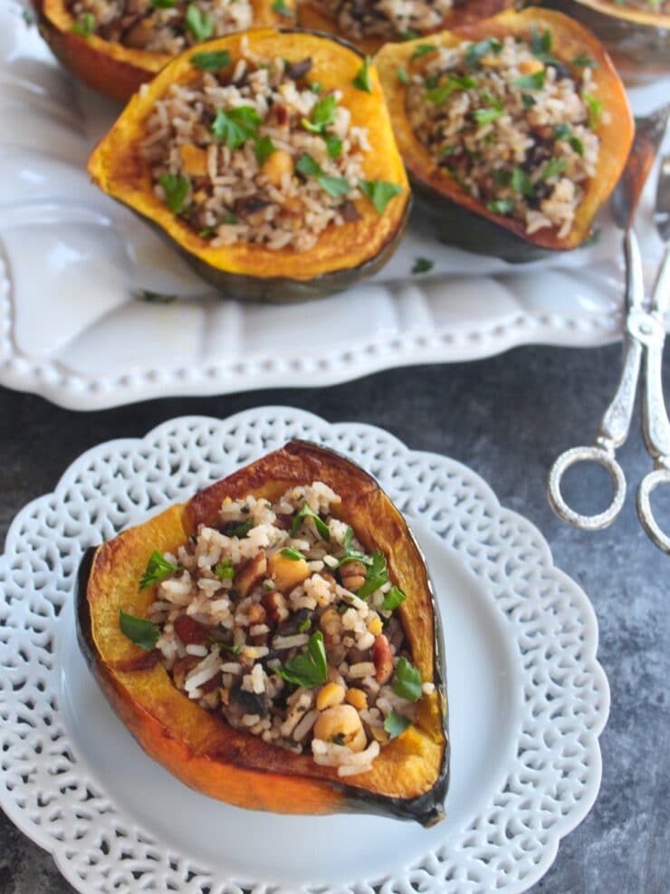 Small decorative plate with stuffed acorn squash, vegan filling - tray of stuffed squash with tongs in the background, on concrete surface