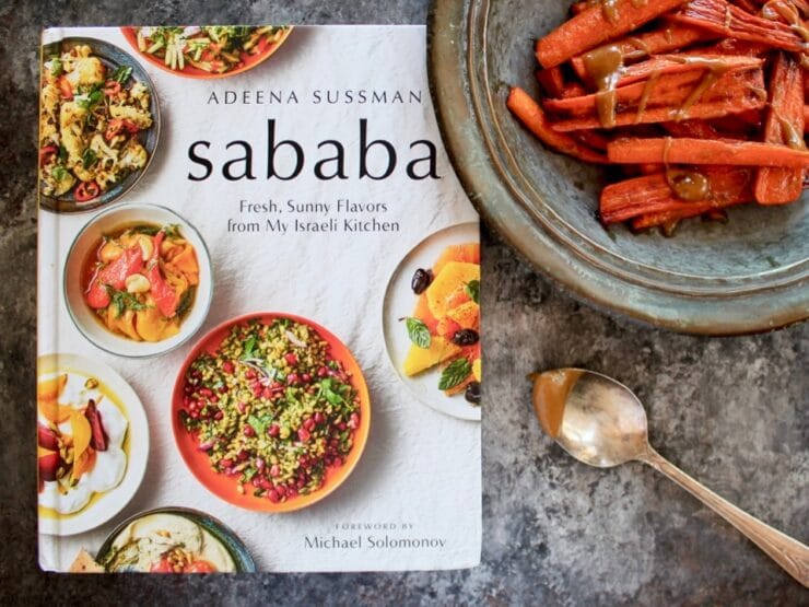 Sababa cookbook with tray of roasted carrots and tahini sauce, spoon on the side.