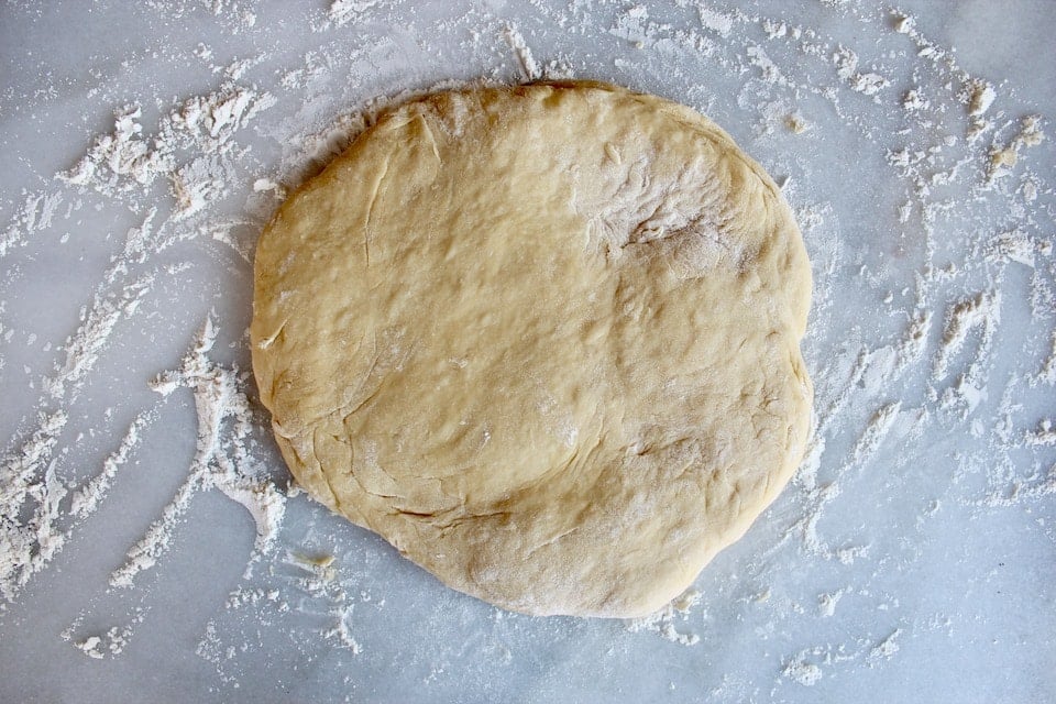 Dough rolled and stretched into a circle on floured marble board.