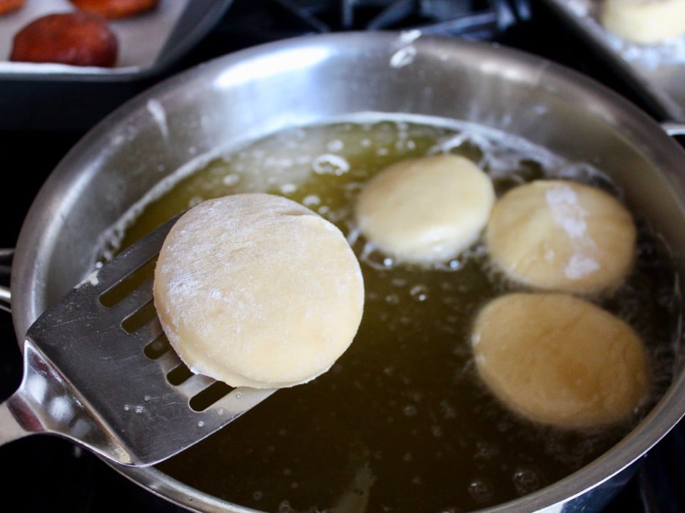 Puffy risen dough circles being gently placed in bubbling oil with spatula.