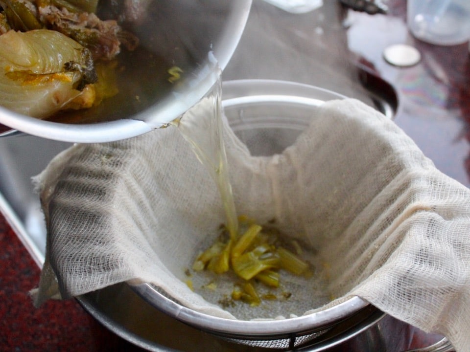 Straining chicken stock through cheesecloth lined mesh strainer.