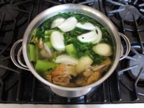 Pot of chicken stock cooking with vegetables and a roast chicken carcass.