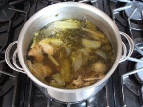 Pot of cooked chicken stock with carcass and cooked vegetables.
