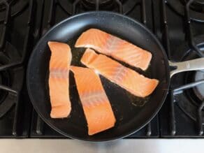 Four skinless salmon fillets face-down in a skillet on stovetop.