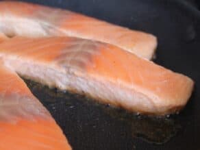 Skinless salmon fillets searing in skillet, close up of bottom of fillet as it begins to brown.
