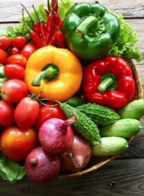 Horizontal image of a bowl, sitting on a wooden table, filled with an assortment of fresh, colorful vegetables.