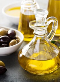 Horizontal shot of a glass bottle filled with olive oil sitting next to a white dish of green and black olives.